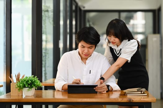 Shot of Asian female office worker pointing at digital tablet screen, discussing on new project with colleague.