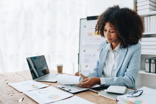 Beautiful young African american businesswoman using laptop computer and paperworks with planning working on financial document, tax, exchange, accounting and Financial advisor.