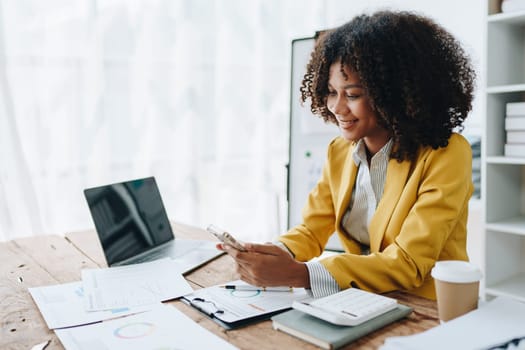 Woman American African using smart phone mobile and laptop computer with planning working on financial document, tax, exchange, accounting and Financial advisor.