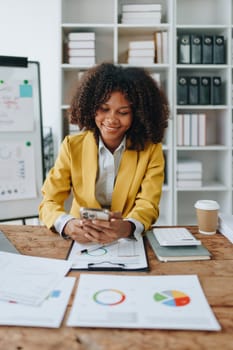 Woman American African using smart phone mobile and laptop computer with planning working on financial document, tax, exchange, accounting and Financial advisor.