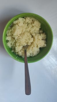 boiled couscous porridge in a green deep plate with a spoon, homemade food. High quality photo