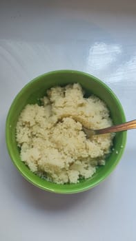 boiled couscous porridge in a green deep plate with a spoon, homemade food. High quality photo