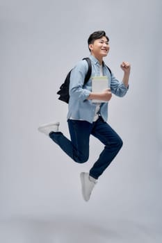 Full length portrait of a smiling young man dressed carrying backpack isolated, holding books, jumping