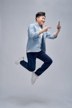 Full length portrait of a joyful young casual man jumping and pointing index finger on mobile phone