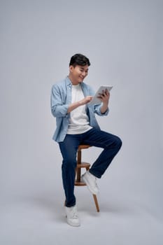 Handsome attractive smiling happy young male using tablet and sitting on the chair 