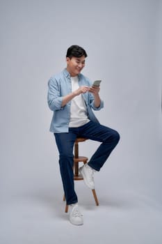 Young man using smartphone, chatting online, browsing social media, sitting on chair 