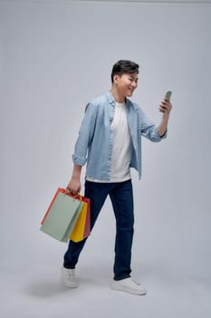 Young Asian man with shopping bags is using a mobile phone and smiling while doing shopping