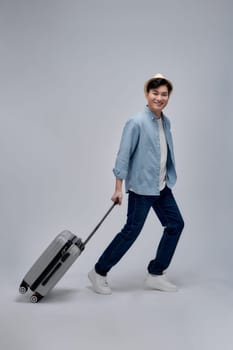 Full length profile shot of a guy walking and pulling a suitcase isolated on white background