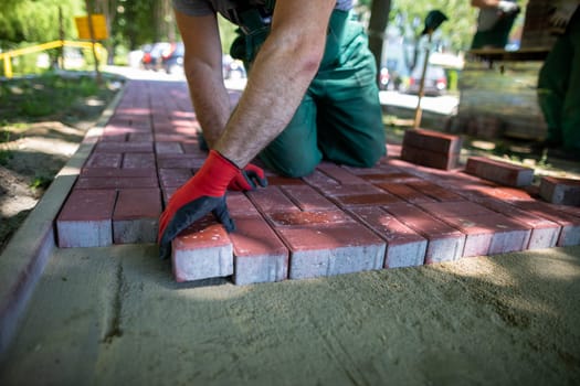 On a hot summer day, a worker manually lays a paving pustule on a newly prepared site. Heavy and demanding construction work.