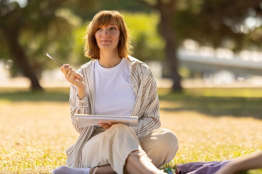 Adult pretty woman sitting in the blooming park holding a painting brush. Mid shot