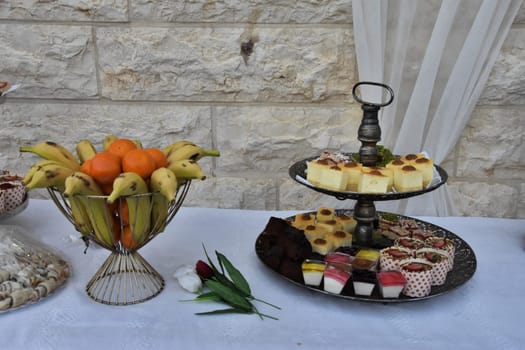 cakes on a platter, bananas in a vase, a bouquet of tulip flowers on a table with a white tablecloth. High quality photo