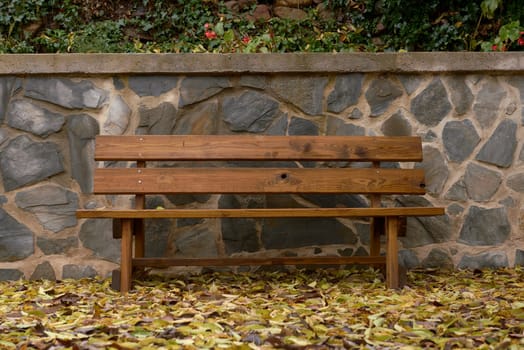 A lonely wooden bench on an autumn day. No one, empty space, orange, ochre and red colours, stone wall, damp,