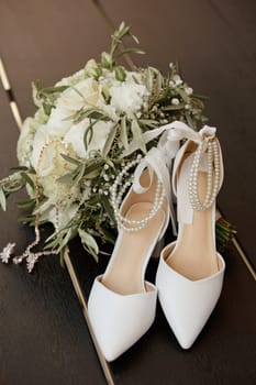Women's shoes of the bride and a wedding bouquet on a wooden background. Soft focus.