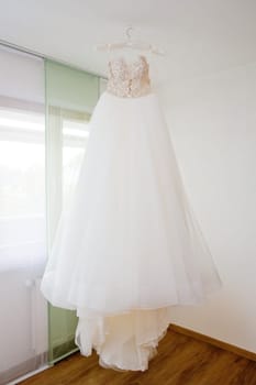 The delicate bride's dress is hanging in room. Selective focus.