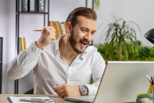 Lebanese businessman working on laptop at home office desk typing browsing say Wow yes found out great big lottery jackpot win, good job news, celebrating. Manager freelancer arab man
