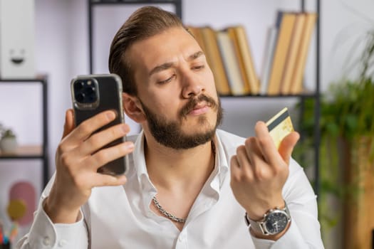 Bearded businessman programmer software developer working making online purchase payment shopping with credit bank card and use laptop at home office desk with laptop. Lebanese freelancer business man