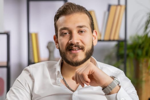 Portrait of happy smiling bearded middle eastern businessman at modern home office workplace desk looking at camera. Male in formal shirt. Man guy remote distant online working on laptop