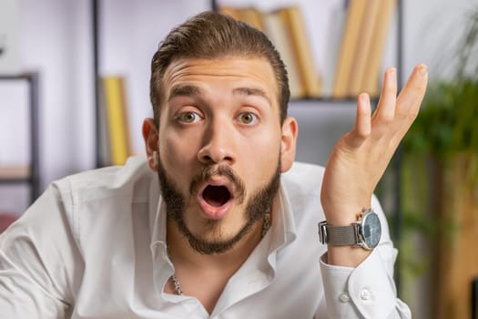 Oh my God, Wow. Lebanese businessman working at home office workplace, looking at camera shocked by sudden victory, game winning, lottery goal achievemen good news. Professional manager freelancer man