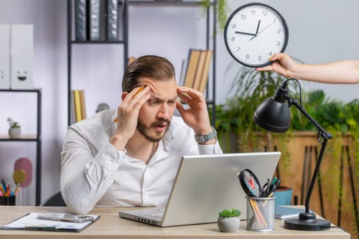Middle eastern businessman working on office laptop with anxiety checking time on clock, running late to work being in delay deadline. Freelancer man looking at hour, minutes worrying to be punctual