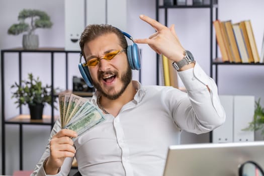 Lebanese businessman holding fan of cash money dollar banknotes celebrate, dance, success career, lottery jackpot game winner, big income, wealth at home office workplace desk. Remote distant working