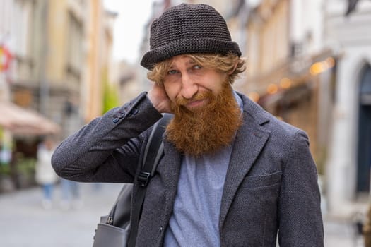 Sad unhappy young bearded man thinks over life concerns, suffers from unfair situation. Problem, feeling bad, annoyed, burnout, grief. Frustrated depressed lonely redhead guy walking in city street