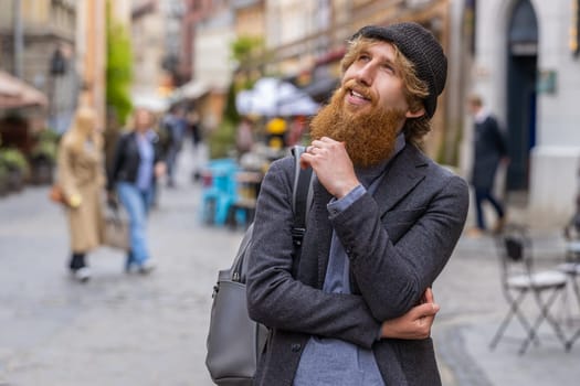 Thoughtful pensive puzzled man with pensive expression, pondering a solution, doubting question, thinking inspiration dreaming outdoors. Redhead guy in city street pointing empty place. Copy-space