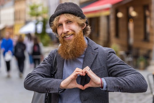 I love you. Bearded man makes symbol of love, showing heart sign to camera, express romantic feelings, express sincere positive feelings. Charity, gratitude, donation. Outdoors in urban city street