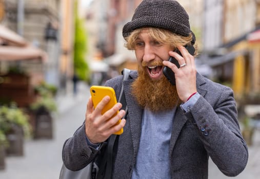 Irritated nervous stressed business man talking screaming on two mobile phones having conversation conflict quarrel complaint dispute discuss solve problem outdoors. Guy walking in urban city street