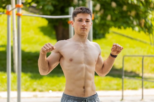 Athletic caucasian topless muscular man stretching body, warm up before cardio workout exercises. Young guy on playground. Sports, health, fitness routine workout. Strength and motivation. Outdoor gym