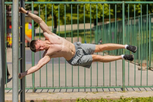 Athletic caucasian topless muscular man doing human flag exercise, strength gymnastics elements. Young shirtless guy on playground. Sports health fitness routine, workout. Motivation. Outdoors gym