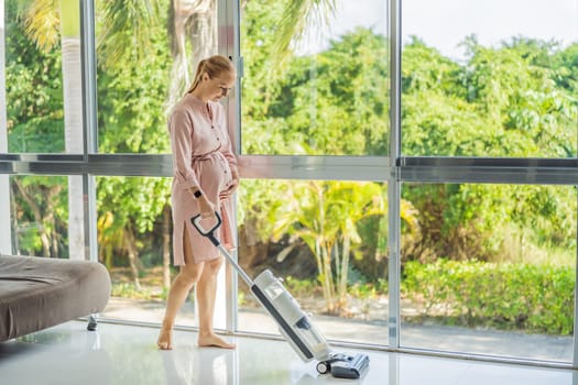 Young pregnant woman enjoys cleaning her house. Easy cleaning with a wireless vacuum cleaner. Pregnant woman cleaning floor with handheld vacuum cleaner. Modern easy cleaning.