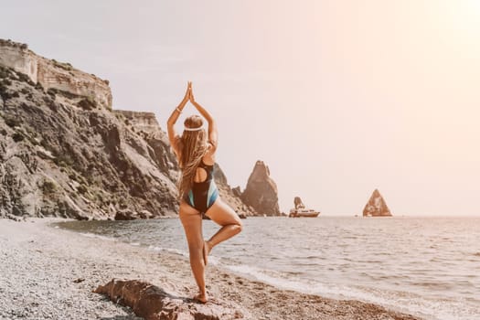 Yoga on the beach. A happy woman meditating in a yoga pose on the beach, surrounded by the ocean and rock mountains, promoting a healthy lifestyle outdoors in nature, and inspiring fitness concept