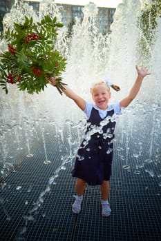 Little girl of elementary school student in modern school uniform outdoors near the fountain water jets. Female child schoolgirl having fun. Back to school in september 1