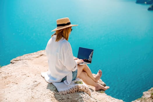 Freelance woman working on a laptop by the sea, typing away on the keyboard while enjoying the beautiful view, highlighting the idea of remote work