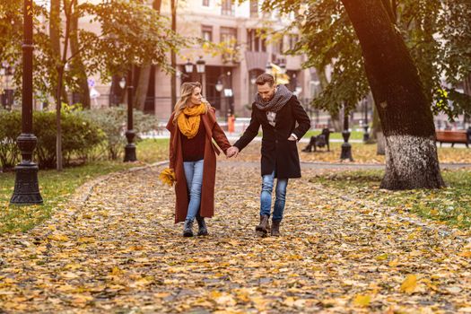 Couple walking in the park holding hands. Outdoor shot of a young couple in love walking along a path through a autumn park. Autumn toned image. 