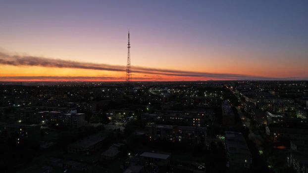 The outskirts of the city. There are old houses, garages and fences. In the distance, you can see the TV tower and the city. Swifts fly. The sky is shimmering purple-blue. Shooting from a drone.