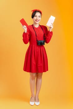 Travel concept. Young happy female Asian tourist holding passport with flight tickets, isolated on orange background