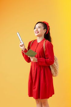 Happy young woman holding tickets and passport to travel isolated on orange background.