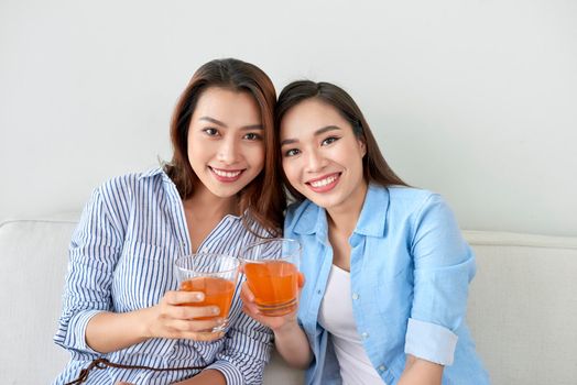 Two sisters on the sofa with orange juice in hands. Two best friends enjoying time.