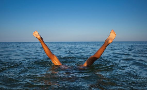 Relaxation and healthy lifestyle. Young boy teenager bathes in the sea. The boy dives and his legs stick out above the water