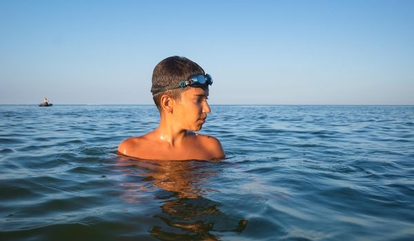 Relaxation and healthy lifestyle. Young boy teenager bathes in the sea.