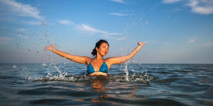 Relaxation and healthy lifestyle. Young beautiful and emotional woman swims in the sea on a sunny day