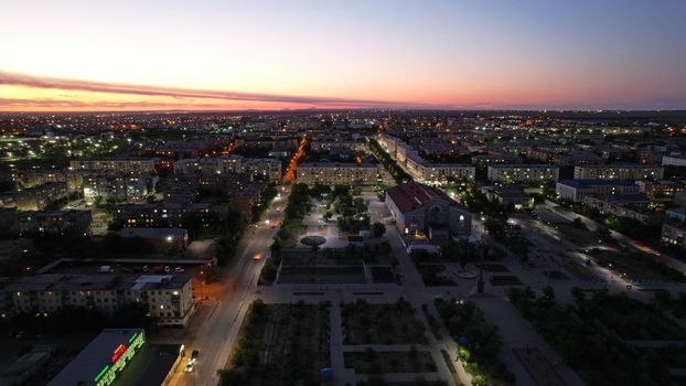 The outskirts of the city. There are old houses, garages and fences. In the distance, you can see the TV tower and the city. Swifts fly. The sky is shimmering purple-blue. Shooting from a drone.