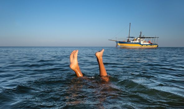 Relaxation and healthy lifestyle. Young boy teenager bathes in the sea. The boy dives and his legs stick out above the water