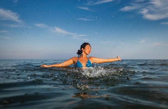 Relaxation and healthy lifestyle. Young beautiful and emotional woman swims in the sea on a sunny day