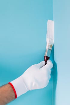 Image of man holding paintbrush and painting blue wall.