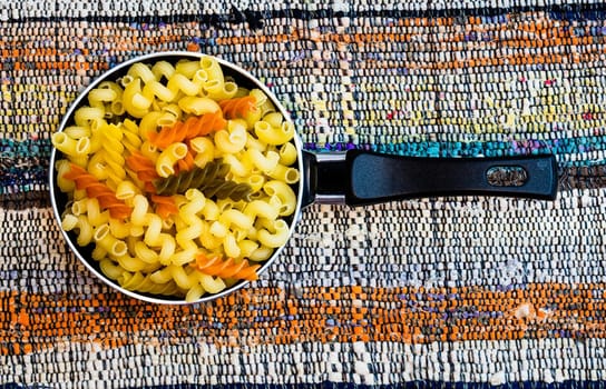 Small mini frying pan with tricolor raw fusilli pasta in a rustic composition.