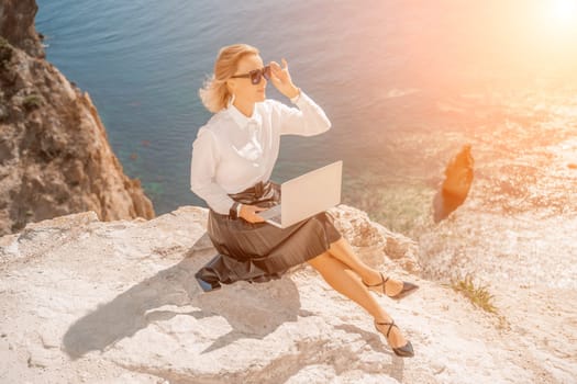 Business woman on nature in white shirt and black skirt. She works with an iPad in the open air with a beautiful view of the sea. The concept of remote work