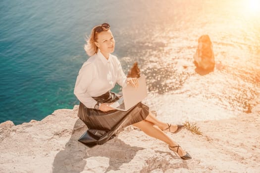 Business woman on nature in white shirt and black skirt. She works with an iPad in the open air with a beautiful view of the sea. The concept of remote work