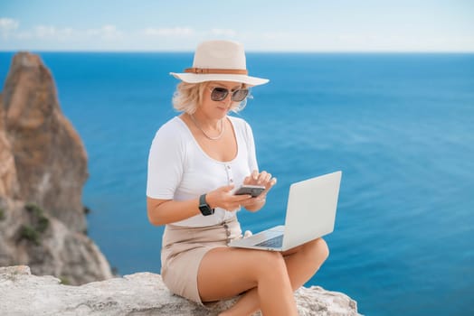 Freelance women sea working on the computer. Good looking middle aged woman typing on a laptop keyboard outdoors with a beautiful sea view. The concept of remote work